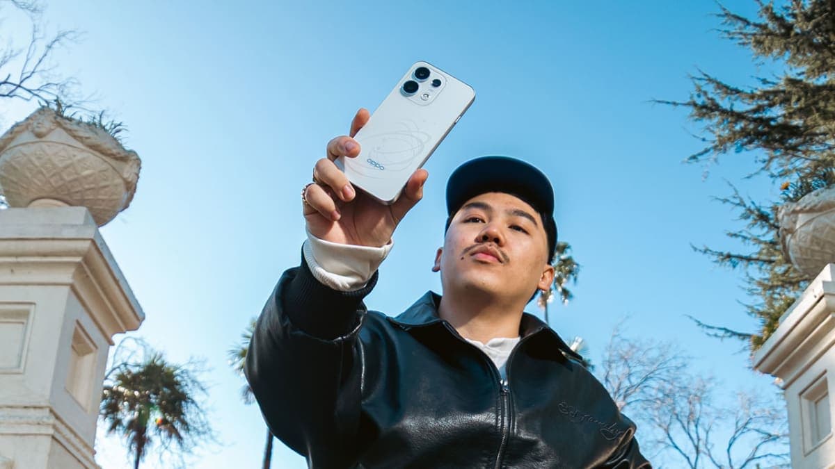 Person taking a rear-camera selfie with a white OPPO Reno16 while sitting on outdoor steps